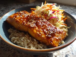 Close-up of a delicious salmon bowl featuring glazed salmon topped with sesame seeds, brown rice, and a side of colorful coleslaw.