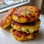 A stack of four golden brown, pan-fried mashed potato cakes garnished with chives.