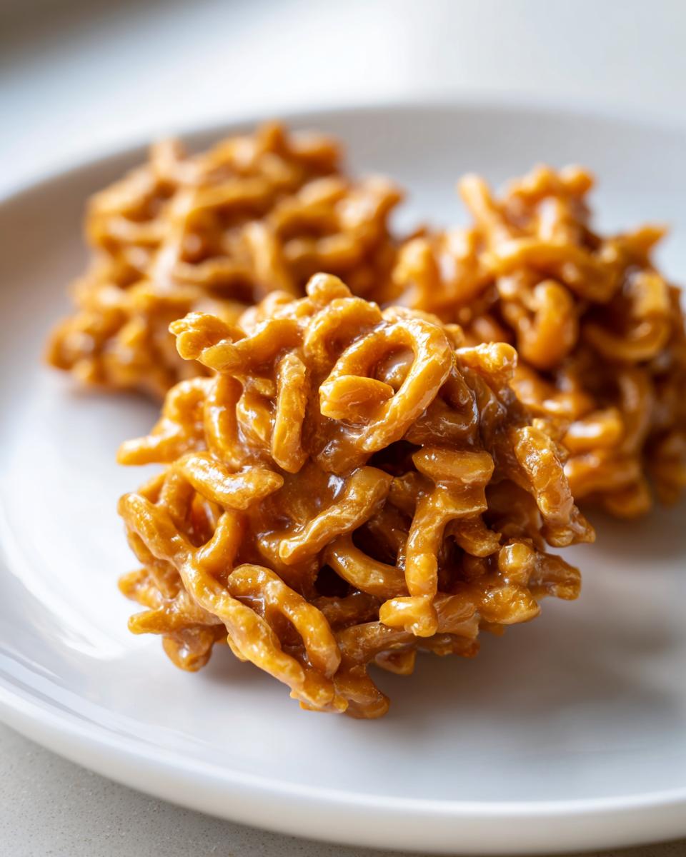 Close-up of three golden brown, glossy haystack cookies resting on a white plate.