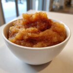 A close-up of chunky, spiced applesauce sprinkled with cinnamon served in a small white bowl.