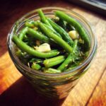 Close-up, overhead shot of bright green dilly beans packed in a glass jar with fresh dill and garlic cloves.