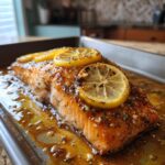 Close-up of a juicy baked salmon recipe fillet topped with caramelized lemon slices and garlic butter sauce.