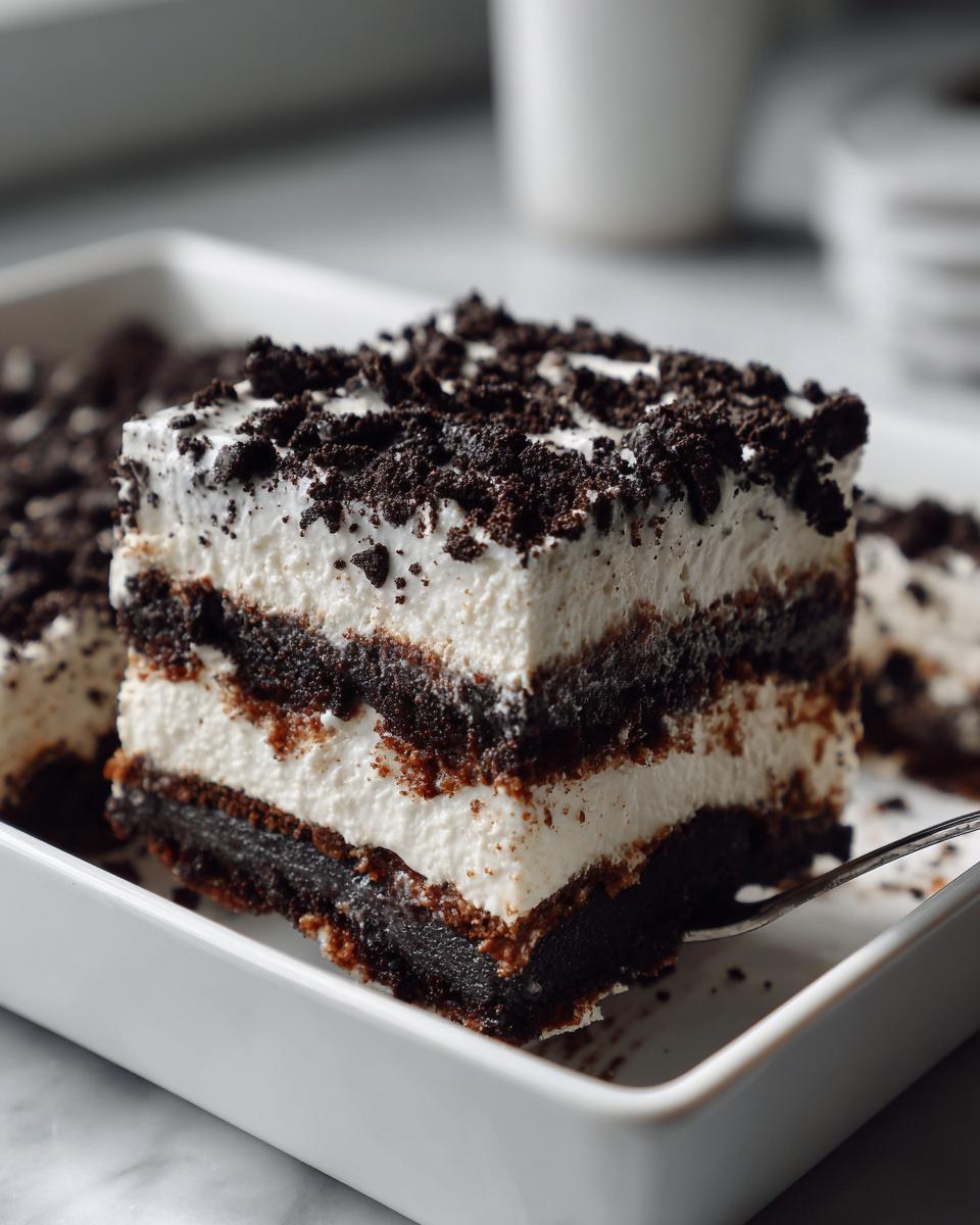 A square slice of layered dirt cake featuring dark chocolate cookie layers and creamy white filling, topped with cookie crumbs.