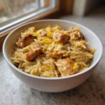 A white bowl filled with creamy lemon chicken orzo, topped with browned chicken pieces and bright lemon zest.