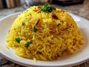 A mound of bright yellow Mediterranean rice garnished with toasted pine nuts and fresh parsley on a white plate.