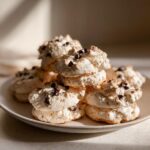 A stack of light, airy meringue forgotten cookies dotted with mini chocolate chips on a ceramic plate.