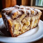 Close-up of a moist slice of apple fritter bread, loaded with apple chunks and drizzled with white icing.