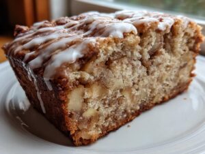 Close-up of a thick slice of moist apple fritter bread, loaded with apple chunks and drizzled with white icing.
