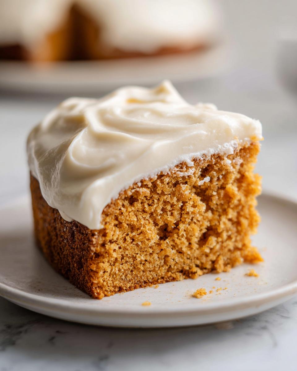 Close-up of a moist slice of applesauce cake topped with thick, swirled cream cheese frosting.