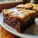Close-up of a moist, dark square of banana bread brownies topped with thick peanut butter-colored frosting.
