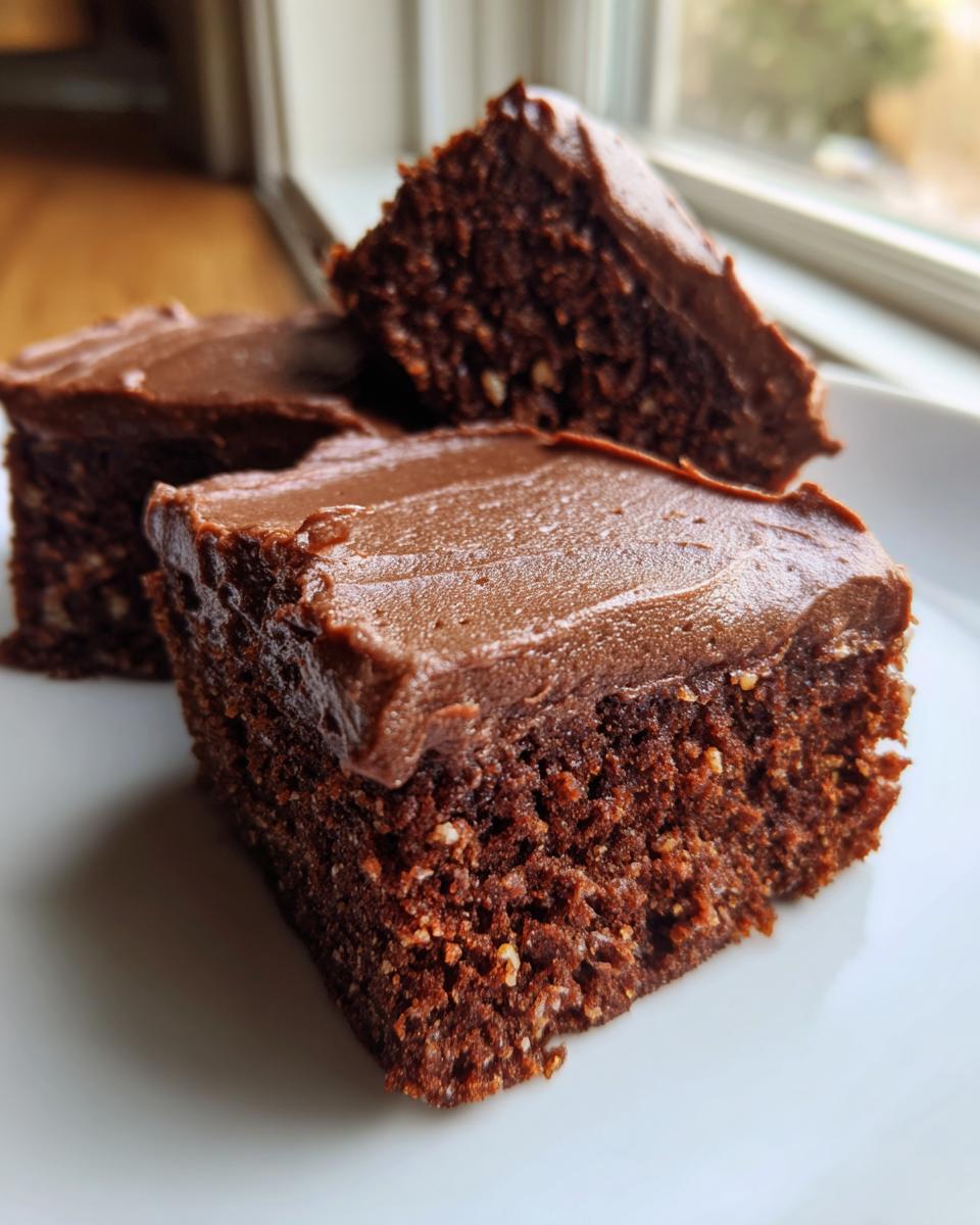 Three squares of moist banana bread brownies topped with rich chocolate frosting on a white plate.