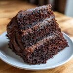 A close-up of a moist slice of dark chocolate cake recipe, layered with rich chocolate frosting.