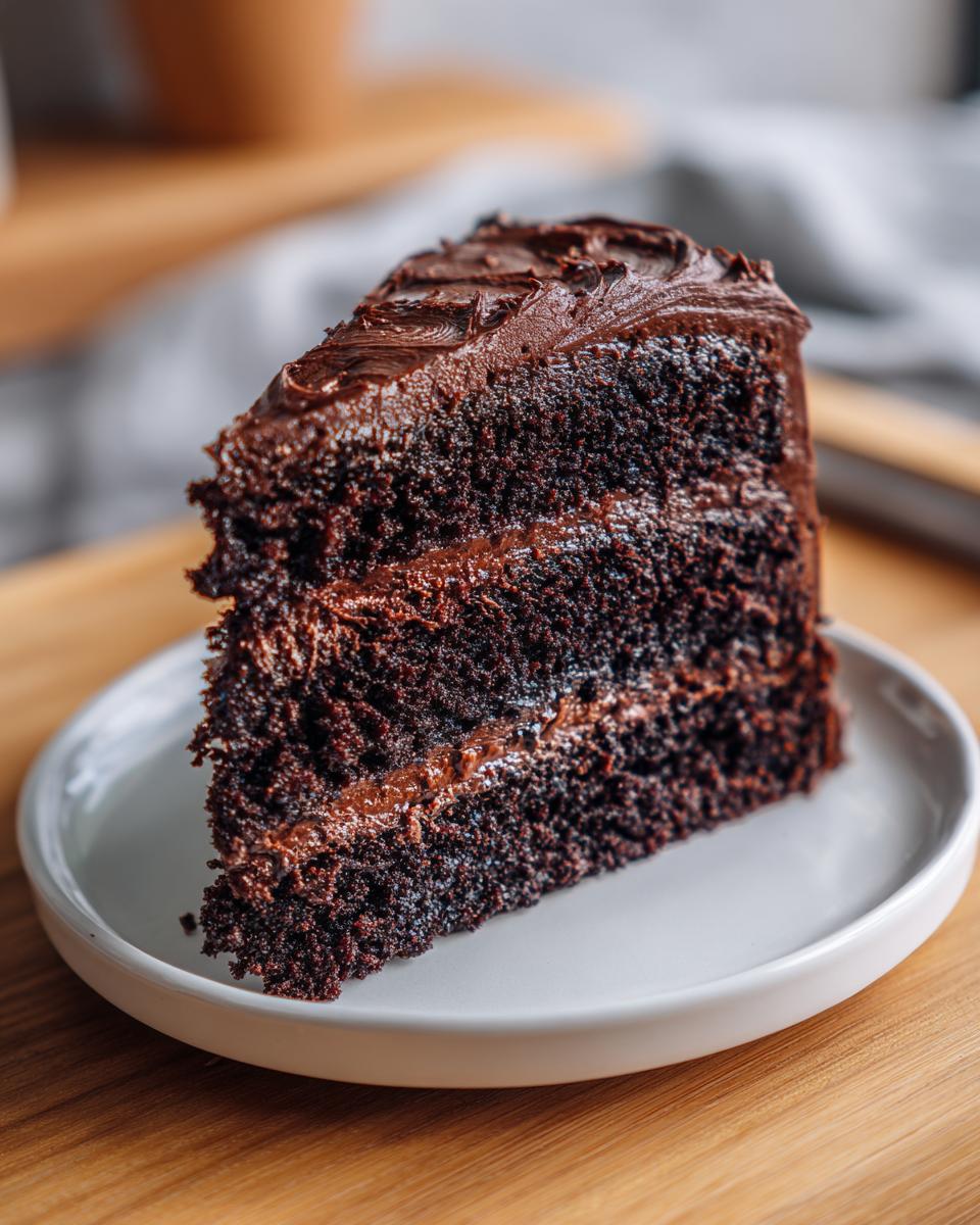 Close-up of a rich, moist slice of three-layer chocolate cake recipe with thick chocolate frosting.