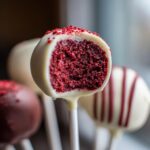 Close-up of a red velvet cake pop cut in half showing the moist interior, coated in white chocolate.