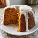 A slice cut from a moist, orange-hued sweet potato pound cake topped with thick white vanilla glaze.
