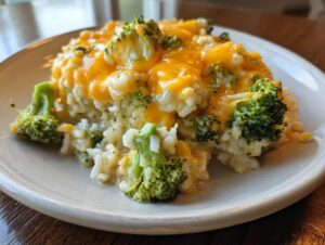 A close-up serving of creamy broccoli rice topped generously with melted cheddar cheese.
