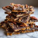 A close-up stack of broken pieces of amazing pecan pie bark, featuring caramel, dark chocolate, and whole pecans.