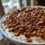 A close-up of a creamy pecan pie dip topped generously with candied pecans and caramel sauce.