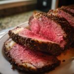 Close-up of thick, medium-rare slices of prime rib roast with a dark, seasoned crust.