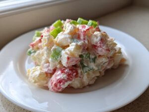 A mound of creamy seafood salad featuring chunks of seafood, red pepper, and green onion served on a white plate.