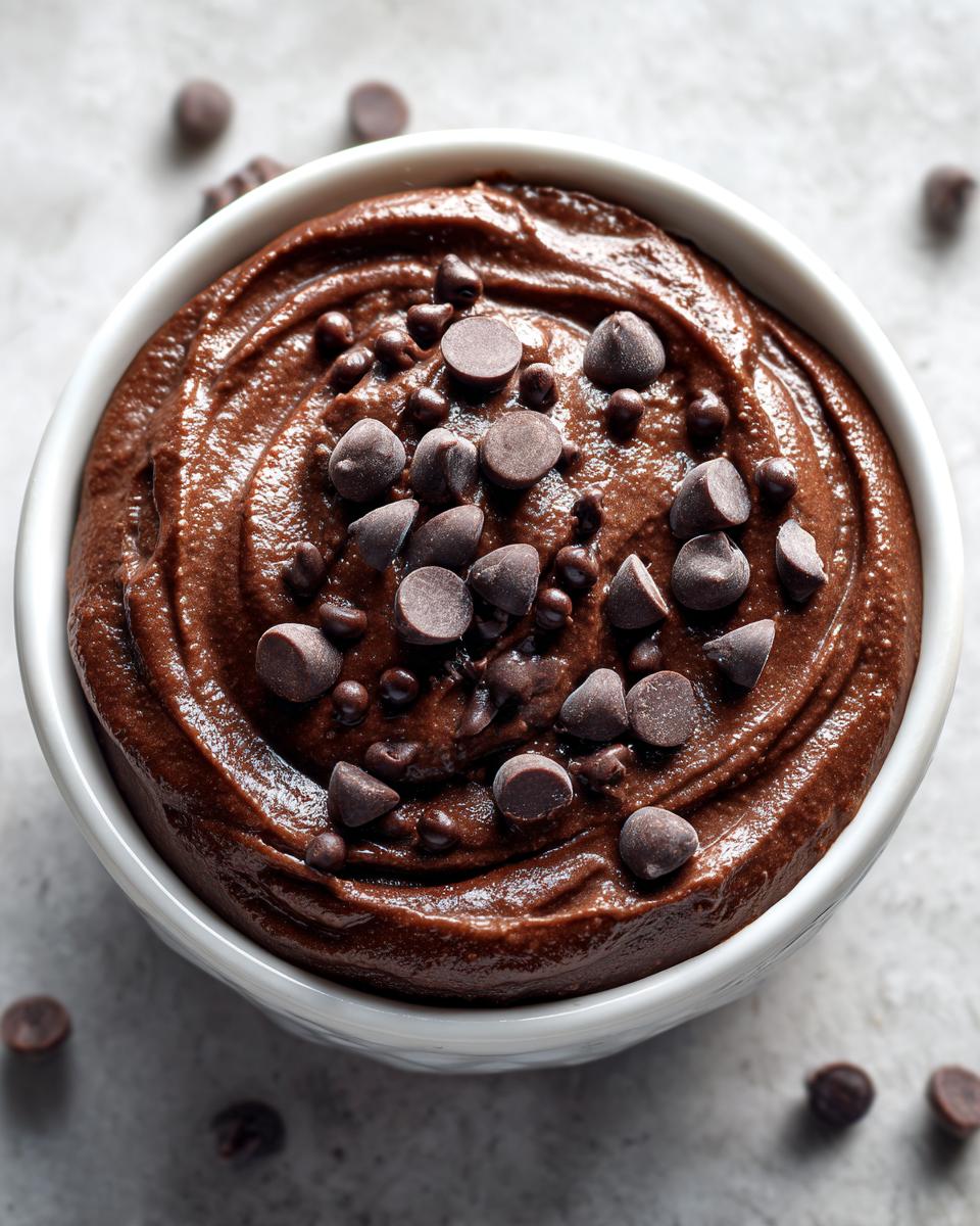 Overhead view of rich, thick brownie batter dip topped with chocolate chips in a white bowl.