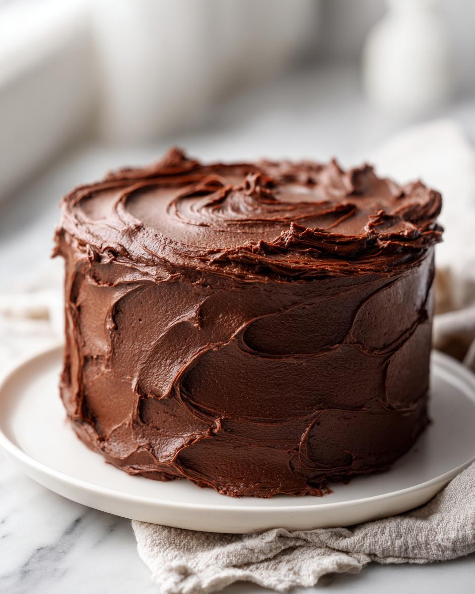 A decadent, tall layer cake completely covered in thick, swirled chocolate frosting.
