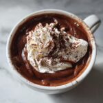Overhead view of a mug filled with thick, rich french hot chocolate topped with whipped cream and cocoa powder.