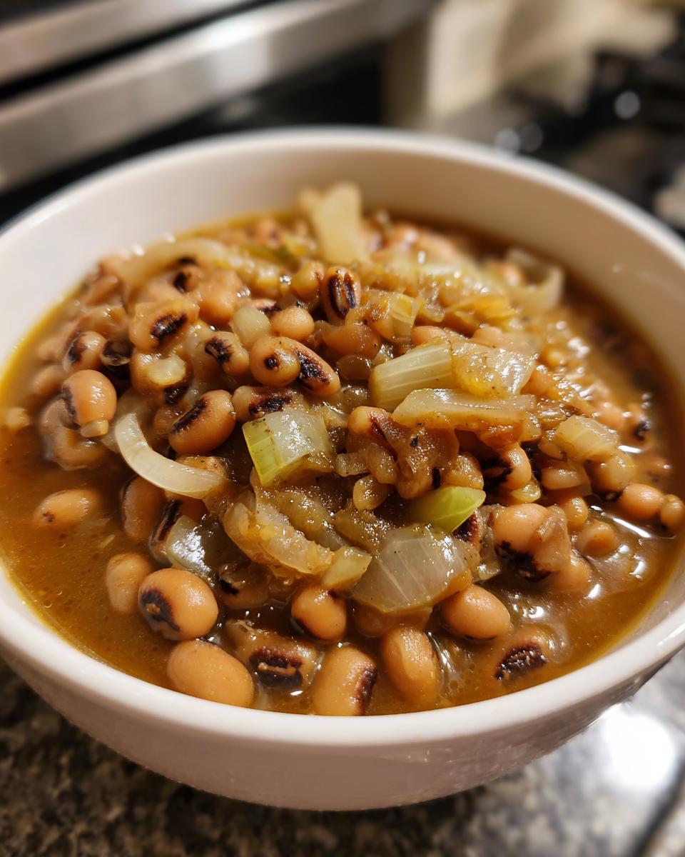 Close-up of a white bowl filled with a rich black eyed peas recipe, featuring tender beans and sautéed onions in a savory broth.