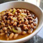 Close-up of a white bowl filled with a savory black eyed peas recipe, featuring tender beans and sautéed onions in broth.