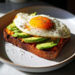 Close-up of savory sweet potato toast topped with mashed sweet potato, sliced avocado, and a sunny-side-up egg.