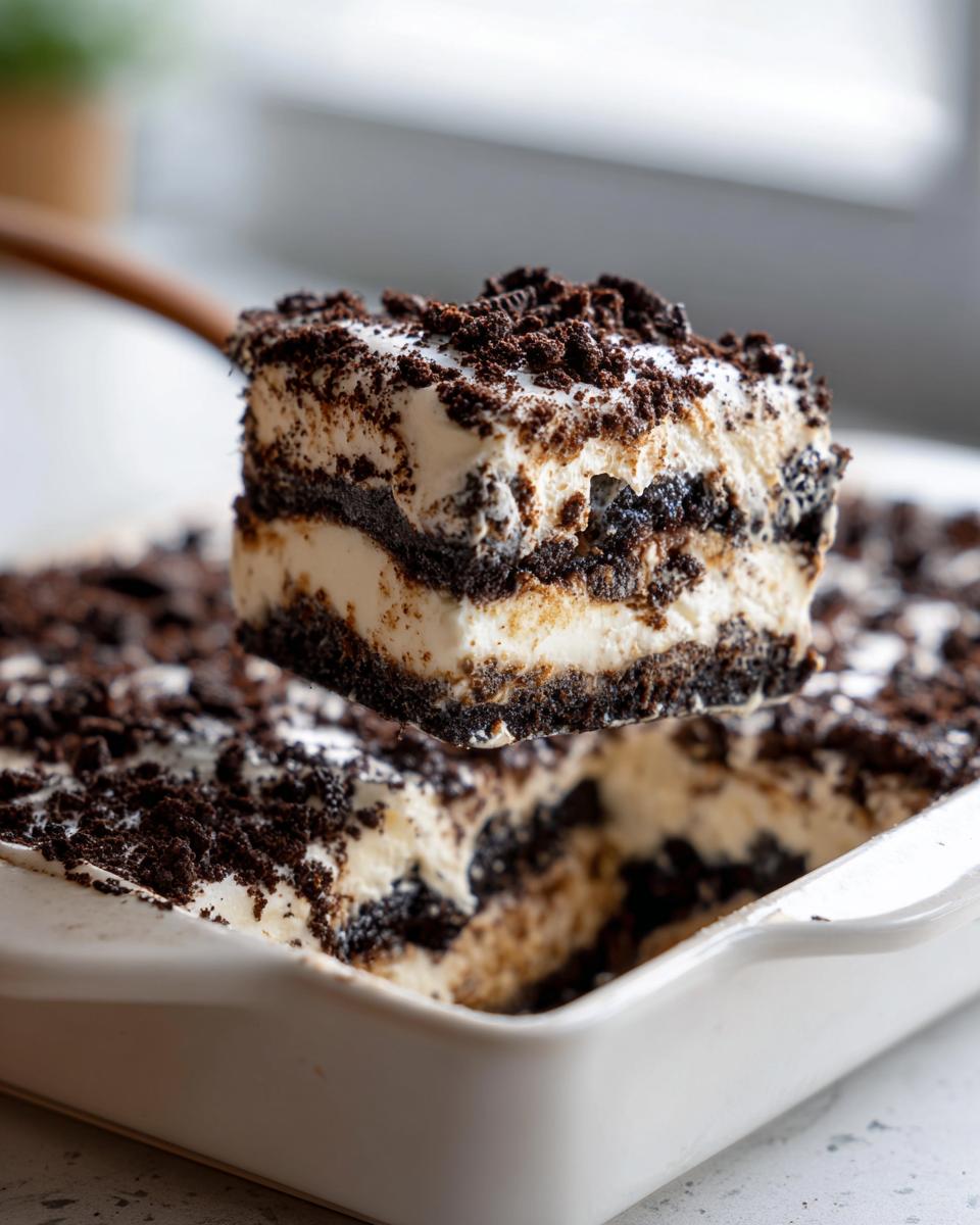 A square slice of rich, layered dirt cake being lifted from a white baking dish with a wooden server.