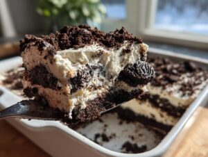 A close-up view of a rich, layered slice of dirt cake being lifted out of a white baking dish with a spatula.