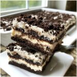 Two stacked slices of decadent dirt cake showing multiple layers of cream and crushed chocolate cookies.