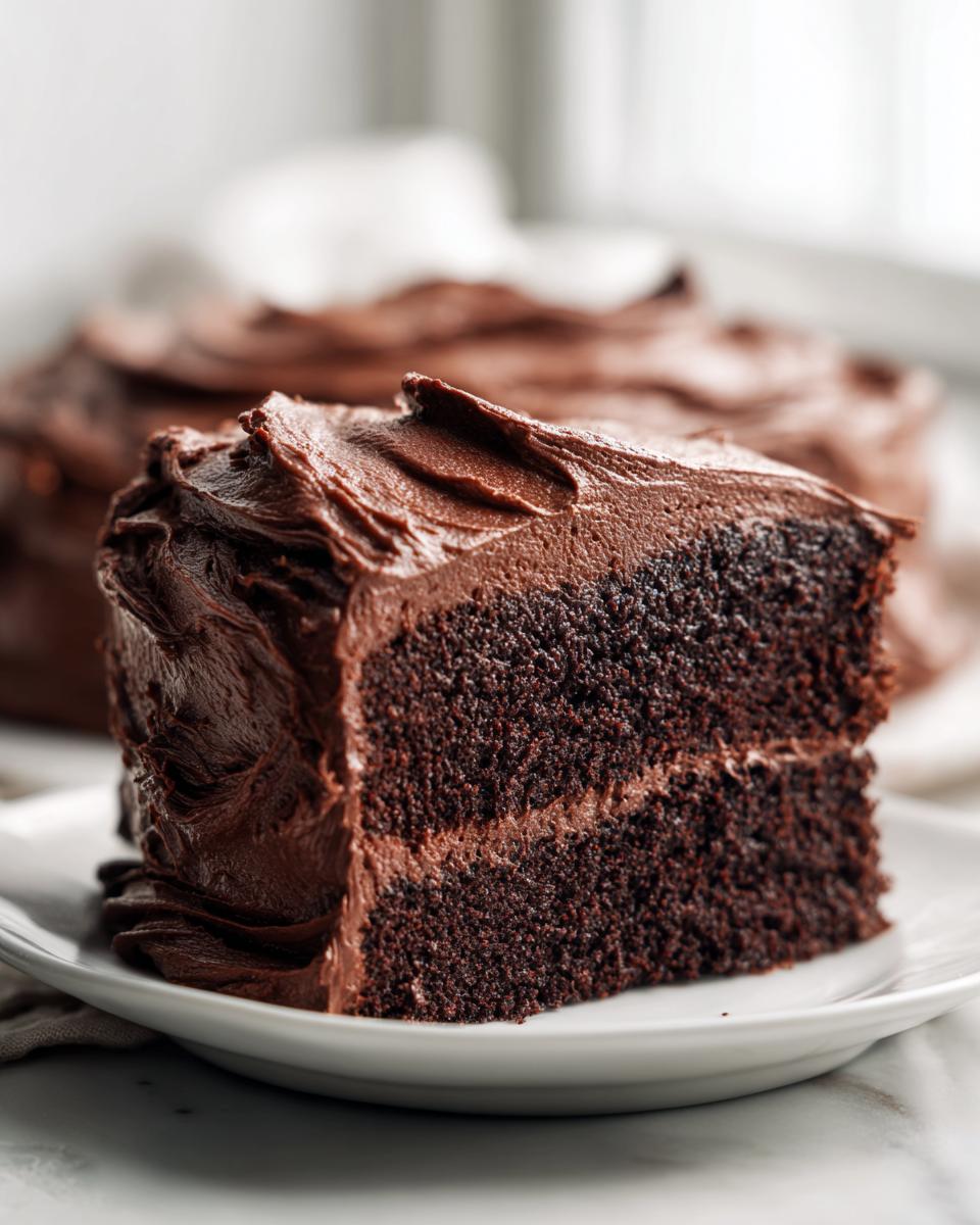 Close-up of a rich slice of dark chocolate cake generously covered in thick chocolate frosting.