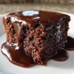 Close-up of a moist slice of chocolate pudding cake generously covered in glossy, dark chocolate sauce.