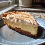 A tempting slice of creamy eggnog pie with a graham cracker crust, topped with whipped cream and cinnamon.