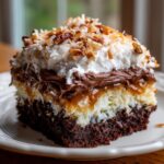 Close-up of a layered slice of german chocolate poke cake showing chocolate cake, coconut filling, caramel, and whipped topping.