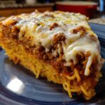 A thick slice of baked spaghetti pie showing layers of spaghetti, meat sauce, and melted mozzarella cheese topping.