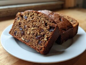 Close-up of three slices of moist date nut bread, rich in dates and walnuts, served on a white plate.