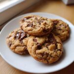 Four freshly baked small batch chocolate chip cookies piled on a white plate.