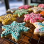 Close-up of snowflake sugar cookies decorated with colorful royal sugar cookie icing recipe, drying on a cooling rack.
