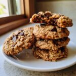 A stack of four soft oatmeal cookie treats, with the top one broken open to show the gooey interior and chocolate chips.