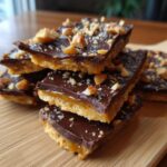 Close-up of stacked squares of homemade toffee recipe with a crunchy base, caramel layer, and chocolate topping sprinkled with nuts.