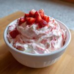 A white bowl filled with fluffy, pink-swirled strawberry cheesecake dip, topped with chopped fresh strawberries.