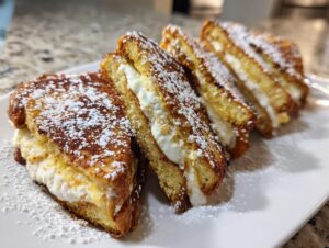 Four golden brown slices of stuffed french toast filled with creamy white filling and dusted with powdered sugar.
