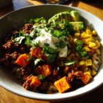 A vibrant sweet potato taco bowl featuring seasoned ground meat, bright orange sweet potato chunks, corn, and topped with sour cream, avocado, and cilantro.