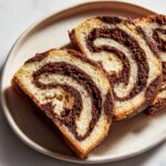 Three slices of chocolate and vanilla swirled pinwheel cookies arranged on a light plate.