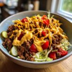 A close-up of a delicious cheeseburger bowl featuring seasoned ground beef, lettuce, tomatoes, pickles, and a generous drizzle of cheese sauce.