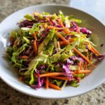 Close-up of a vibrant cabbage salad featuring shredded green and purple cabbage, julienned carrots, and sesame seeds.