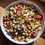 Close-up of a vibrant mediterranean chickpea salad mixed with cucumber, tomatoes, red onion, olives, and feta cheese.